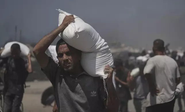 Palestinians carry sacks of flour unloaded from a humanitarian aid convoy that reached Gaza City from the northern Gaza Strip, Sunday, July 27, 2025. (AP Photo/Jehad Alshrafi)