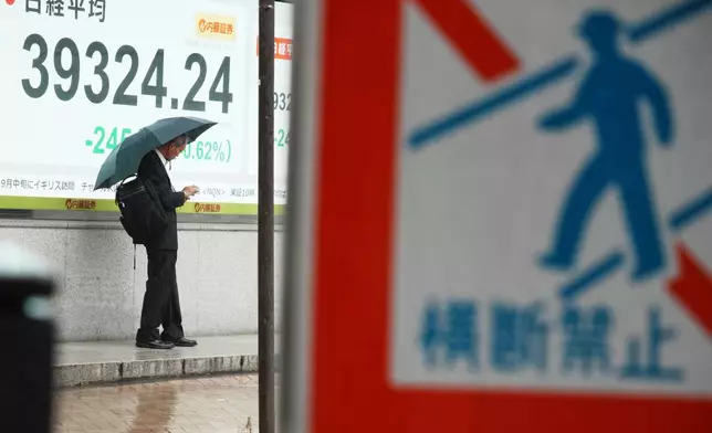 A person stands in front of an electronic stock board showing Japan's Nikkei index at a securities firm Monday, July 14, 2025, in Tokyo. (AP Photo/Eugene Hoshiko)