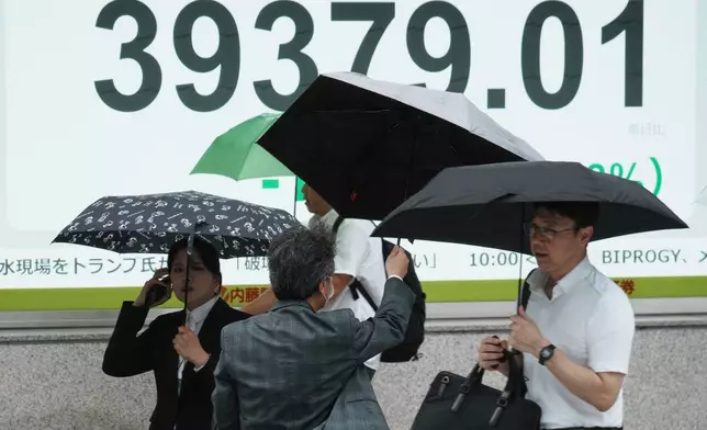 People walk in front of an electronic stock board showing Japan's Nikkei index at a securities firm Monday, July 14, 2025, in Tokyo. (AP Photo/Eugene Hoshiko)