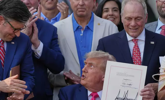 President Donald Trump holds his signed his signature bill of tax breaks and spending cuts at the White House, Friday, July 4, 2025, in Washington, surrounded by members of Congress, as he looks to House Speaker Mike Johnson of La.. (AP Photo/Julia Demaree Nikhinson)