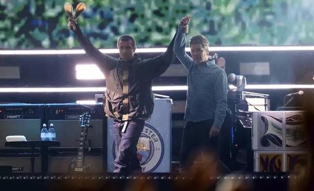 Liam Gallagher, left, holds the hand aloft of Noel Gallagher from the band Oasis as they perform during their reunion concert on Friday, July 4, 2025, in Cardiff. (Photo by Scott A Garfitt/Invision/AP)