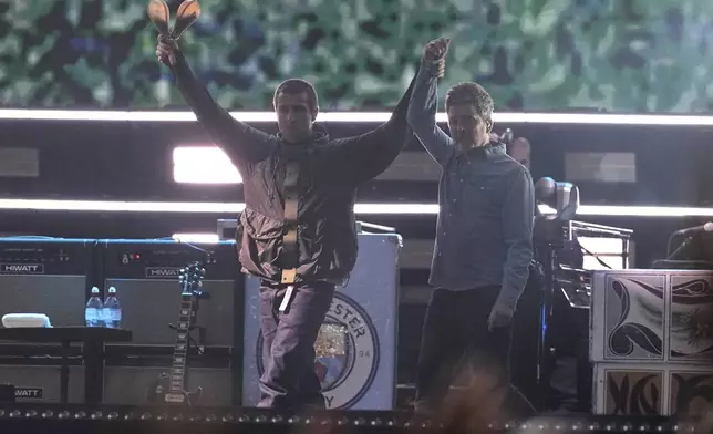 Liam Gallagher, left, holds the hand aloft of Noel Gallagher from the band Oasis as they perform during their reunion concert on Friday, July 4, 2025, in Cardiff. (Photo by Scott A Garfitt/Invision/AP)