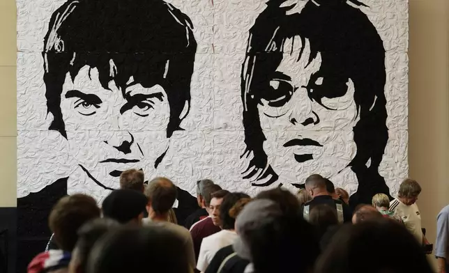 Oasis fans take photos in front of the Wonder Wall - a mural by Welsh artist Nathan Wyburn made out of 3,000 black and white bucket hats depicting Liam and Noel Gallagher - at the St David's shopping centre in Cardiff, ahead of the first show in their long-awaited reunion tour kicking off in Wales, Friday, July 4, 2025. (Jordan Pettitt/PA via AP)