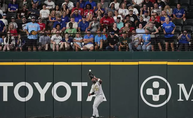 Athletics left fielder Miguel Andujar reaches up to catch a fly out by Texas Rangers' Michael Helman in the first inning of a baseball game, Wednesday, July 23, 2025, in Arlington, Texas. (AP Photo/Tony Gutierrez)