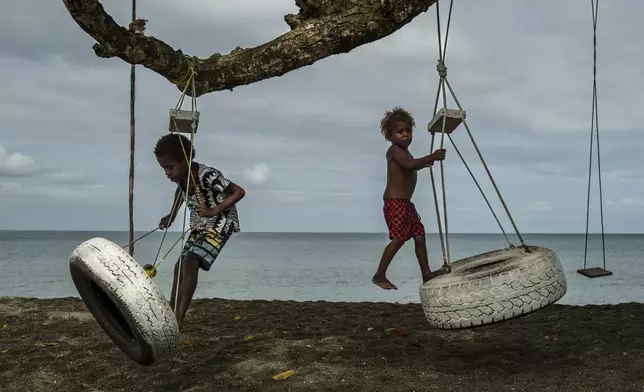 Children play with swings on an uprooted tree along a beach in Mele, Vanuatu, that was once lined with vegetation, now largely lost to storms, erosion and other environmental pressures on Saturday, July 19, 2025. (AP Photo/Annika Hammerschlag)