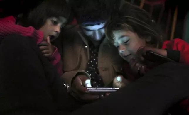 FILE - Children from Yazidi families, displaced by Islamic State group militants, look at a smartphone in a partially constructed building in Dohuk, northern Iraq, Dec. 10, 2014. (AP Photo/Seivan Selim, File)