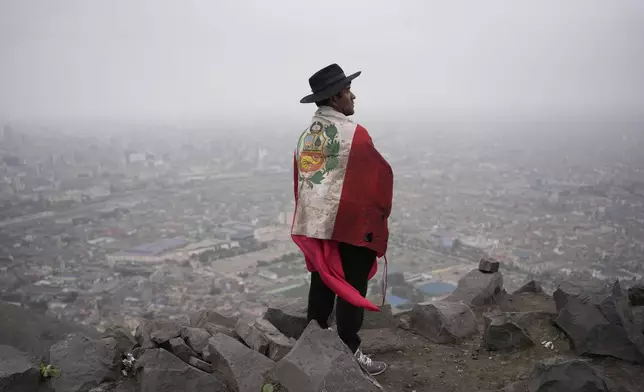 A demonstrator taking part in a march against a recently approved amnesty law that benefits military members and civilians prosecuted for human rights abuses during the country's armed conflict stands on a hill overlooking Lima, Peru, Sunday, July 27, 2025. (AP Photo/Martin Mejia)