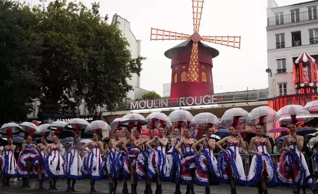 Moulin Rouge cabaret dancers hold umbrellas during the last stage of the Tour de France cycling race between Mantes-la-Ville and Paris, Sunday, July 27, 2025 in Paris (AP Photo/Michel Euler)