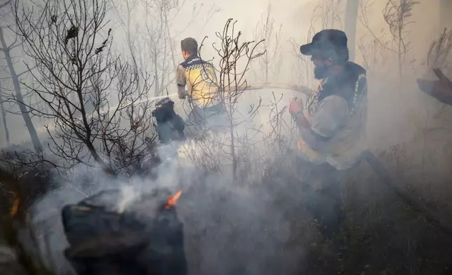 Emergency responders with the Syrian Civil Defense, known as the White Helmets, work to extinguish a wildfire near the town of Rabia, in Syria's Latakia countryside, Sunday, July 6, 2025. (AP Photo/Ghaith Alsayed)