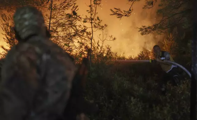 An emergency responder with the Syrian Civil Defense, known as the White Helmets, works to extinguish a wildfire in the town of Rabia, in Latakia province, Syria, Saturday, July 5, 2025. (AP Photo/Ghaith Alsayed)