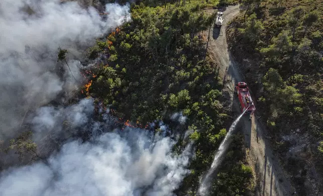 Emergency responders with the Syrian Civil Defense, also known as the White Helmets, work to extinguish a wildfire in the town of Rabia, in the Latakia countryside, Syria, Saturday, July 5, 2025. (AP Photo/Ghaith Alsayed)