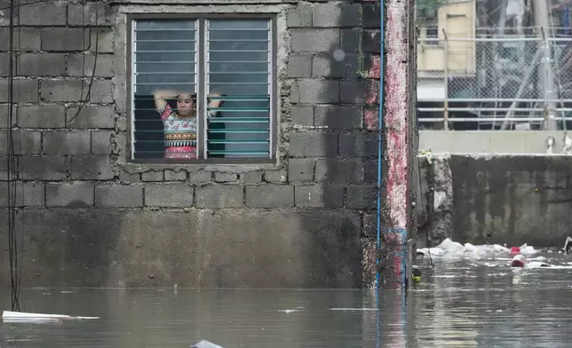 A woman looks outside from her flooded home following tropical storm Wipha fueled monsoon rains in Quezon city, Philippines on Tuesday, July 22, 2025. (AP Photo/Aaron Favila)