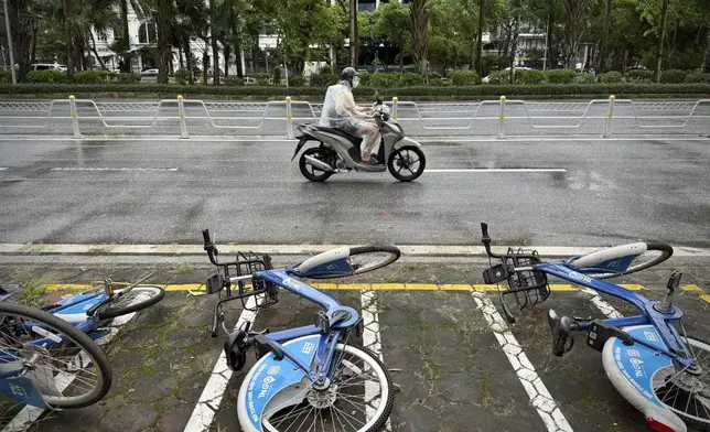 A motorcyclist drives past fallen bicycles in the rain caused by tropical storm Wipha in Hanoi, Vietnam on Tuesday, July 22, 2025. (AP Photo/Huy Han)