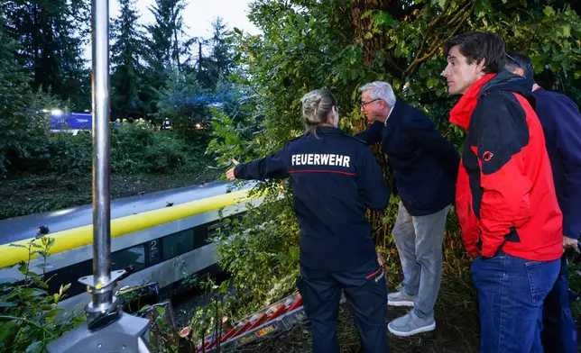 District fire chief of the Biberach district, Charlotte Ziller, left, shows the district administrator of the Biberach district, Mario Glaser, and Interior Minister Thomas Strobel, center, the scene of the derailed regional passenger train accident near Riedlingen, Germany, Sunday, July 27, 2025. (Thomas Warnack/dpa via AP)