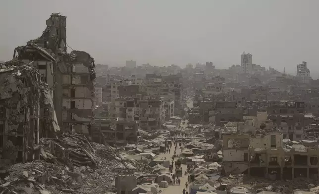 People walk along a street lined with destroyed buildings following Israeli bombardments during the Israel-Hamas war in the Gaza Strip, Tuesday, July 29, 2025. (AP Photo/Jehad Alshrafi)