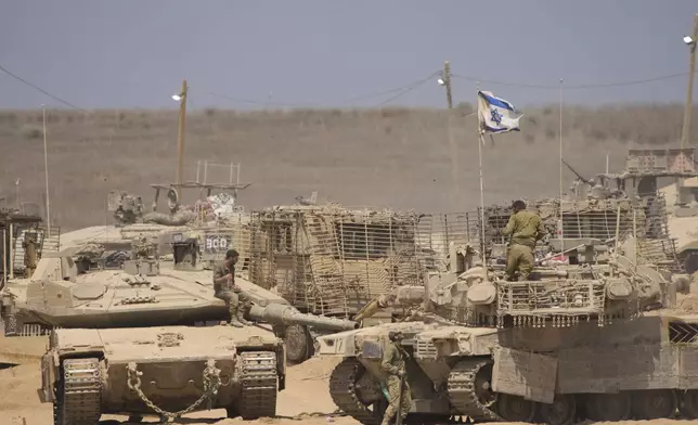 Israeli soldiers work on their tanks in a staging area on the border with Gaza Strip, in southern Israel, Tuesday, July 29, 2025. (AP Photo/Ariel Schalit)