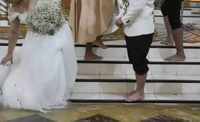 Bride Jamaica Aguilar, left, arranges her gown beside barefoot groom Jade Rick Verdillo, second from right, during their wedding at the flooded Barasoain church in Malolos, Bulacan province, Philippines on Tuesday, July 22, 2025. (AP Photo/Aaron Favila)