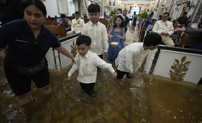 Wedding guests walk inside the flooded Barasoain church in Malolos, Bulacan province, Philippines on Tuesday, July 22, 2025. (AP Photo/Aaron Favila)