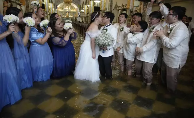 Newlyweds Jade Rick Verdillo, center, and Jamaica pose with a kiss as guests cheer at the flooded Barasoain church in Malolos, Bulacan province, Philippines on Tuesday, July 22, 2025. (AP Photo/Aaron Favila)