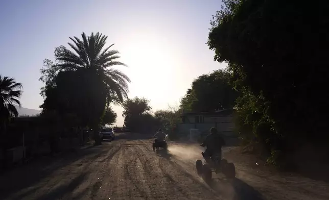 Dust rises as two residents ride ATVs through Oasis Mobile Home Park in Thermal, Calif., Tuesday, April 15, 2025. (AP Photo/Jae C. Hong)