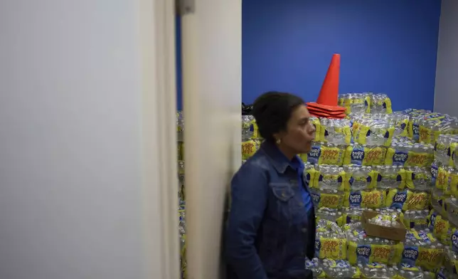 Luz Gallegos, executive director of the immigrant and farmworker justice group TODEC, leans on the door of an office filled with bottled water donated for mobile home residents in Coachella, Calif., Monday, April 14, 2025. (AP Photo/Jae C. Hong)