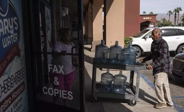Agustin Toledo, a mobile home resident in Southern California's eastern Coachella Valley, pushes a cart carrying empty water jugs into a water store to refill the jugs in Coachella, Calif., Wednesday, Oct. 30, 2024. (AP Photo/Jae C. Hong)