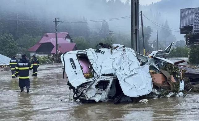 In this image released by the Romanian Emergency Services Suceava (ISU Suceava) first responders walk by damaged vehicles after a flash flood in the village of Brosteni, northern Romania, Monday, July 28, 2025. (Romanian Emergency Services - ISU Suceava via AP)