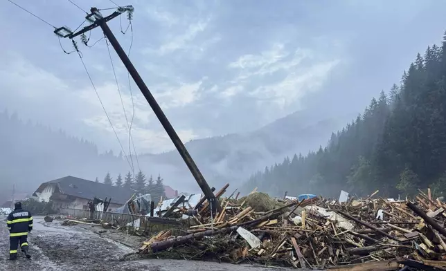 In this image released by the Romanian Emergency Services Suceava (ISU Suceava) first responders walk by damaged vehicles after a flash flood in the village of Brosteni, northern Romania, Monday, July 28, 2025. (Romanian Emergency Services - ISU Suceava via AP)