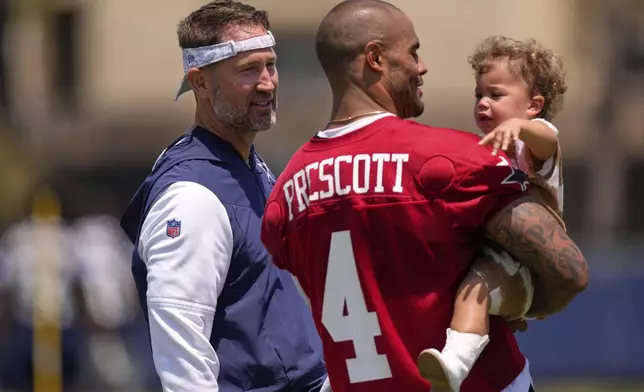 Dallas Cowboys head coach Brian Schottenheimer, left, talks with quarterback Dak Prescott as Prescott holds his daughter Margaret Jane after training camp Tuesday, July 22, 2025, in Oxnard, Calif. (AP Photo/Mark J. Terrill)