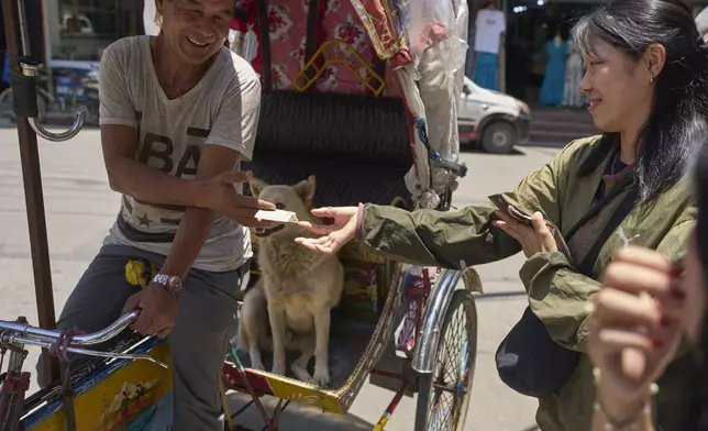 A passenger offers extra tip to Babu Tamang and for his canine Shayam after a ride, in Kathmandu, Nepal, Thursday, July 3, 2025. (AP Photo/Niranjan Shrestha)