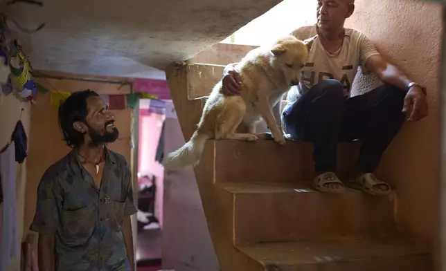 Babu Tamang speaks with his apartment mate as his canine Shayam sits beside him in their small rented house in Kathmandu, Nepal, Thursday, July 24, 2025. (AP Photo/Niranjan Shrestha)