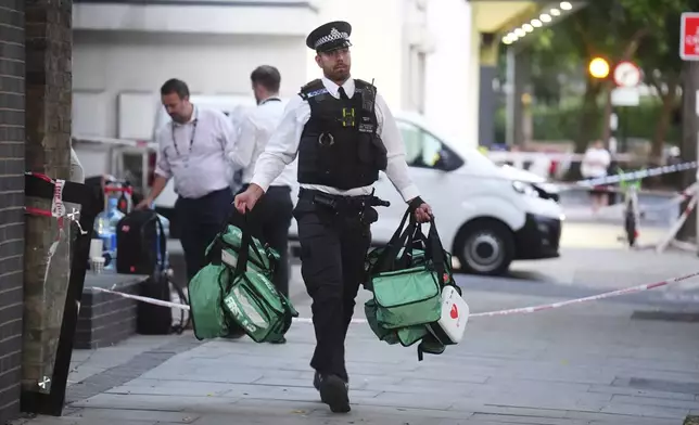 A police officer removes medical bags from the scene in Southwark, south London, Monday, July 28, 2025, where four people were stabbed earlier today. (James ManningPA via AP)