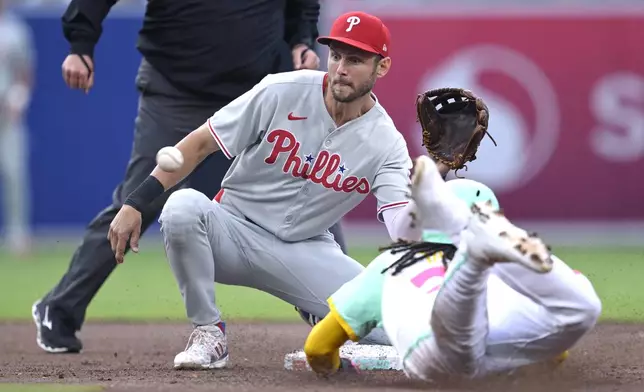 San Diego Padres' Fernando Tatis Jr., right, steals second base as the throw gets away from Philadelphia Phillies shortstop Trea Turner, front left, during the second inning of a baseball game Friday, July 11, 2025, in San Diego. (AP Photo/Orlando Ramirez)