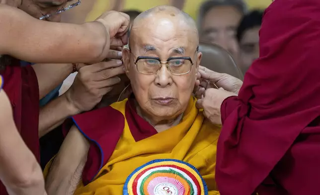 Attendant monks help put a microphone on the spiritual leader of Tibetan Buddhists, the Dalai Lama, during his 90th birthday celebration at the Tsuglakhang temple in Dharamshala, India, Sunday, July 6, 2025.(AP Photo/Ashwini Bhatia)