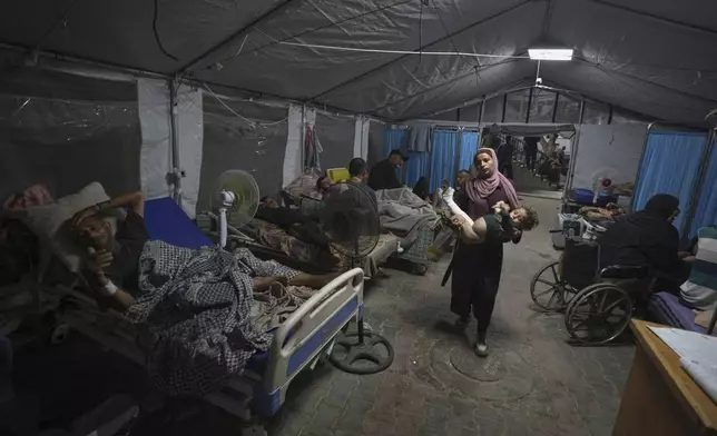 A mother carries her child into a patient treatment tent set up in the yard of Shifa Hospital in Gaza City, Friday, July 4, 2025. (AP Photo/Jehad Alshrafi)
