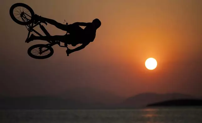 A youth rides his BMX bike to perform a jump into the sea during a hot day at Kavouri beach, south of Athens, Greece, Saturday, July 19, 2025. (AP Photo/Yorgos Karahalis)