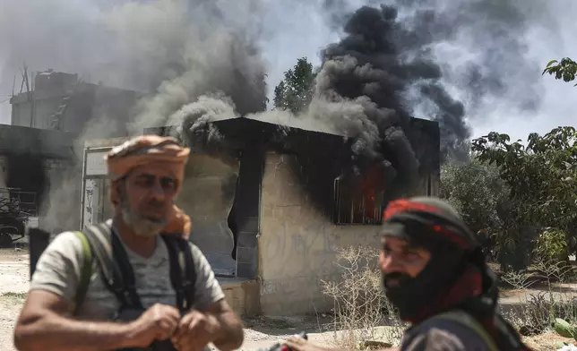 Bedouin fighters stand in front a burned shop at Mazraa village on the outskirts of Sweida city, during clashes between the Bedouin clans and Druze militias, southern Syria, Friday, July 18, 2025. (AP Photo/Ghaith Alsayed)