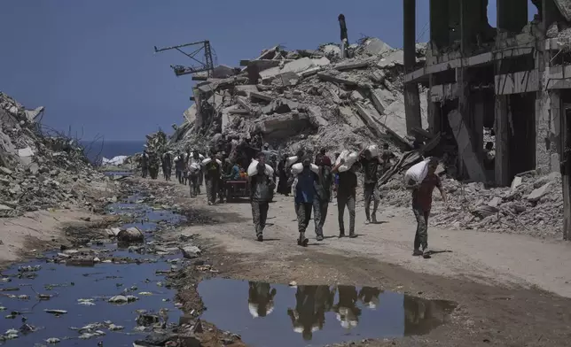 Palestinians carry sacks of flour unloaded from a humanitarian aid convoy that reached Gaza City from the northern Gaza Strip, Tuesday, July 22, 2025. (AP Photo/Jehad Alshrafi)
