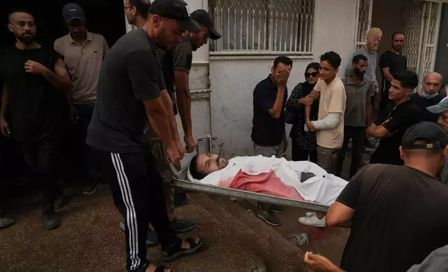 EDS NOTE: GRAPHIC CONTENT - Palestinians carry the body of a member of their family, who was killed while trying to reach aid trucks entering northern Gaza through the Zikim crossing with Israel, at the morgue of the Shifa Hospital, in Gaza City, Saturday, July 26, 2025. (AP Photo/Abdel Kareem Hana)