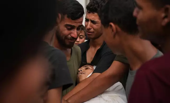 Palestinians mourn over the body of a member of their family, who was killed while trying to reach aid trucks entering northern Gaza through the Zikim crossing with Israel, at Shifa Hospital, in Gaza City, Saturday, July 26, 2025. (AP Photo/Abdel Kareem Hana)
