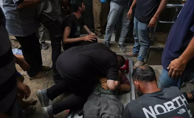 Palestinians mourn over the body of a member of their family, who was killed while trying to reach aid trucks entering northern Gaza through the Zikim crossing with Israel, at Shifa Hospital, in Gaza City, Saturday, July 26, 2025. (AP Photo/Abdel Kareem Hana)