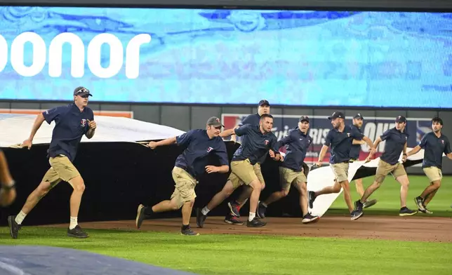 Grounds crews scramble to roll out the tarp as a storm delays the game between the Minnesota Twins and the Boston Red Sox during the ninth inning of a baseball gam,e Monday, July 28, 2025, in Minneapolis. (AP Photo/Craig Lassig)