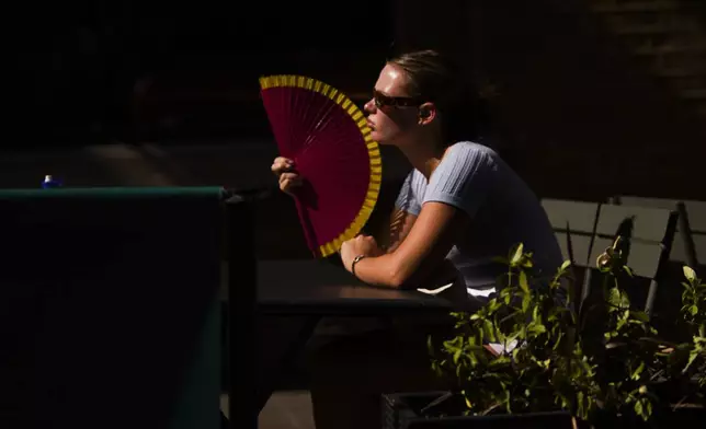 A woman holds a fan in hot weather while sitting at a table in Covent Garden, in London, Monday, June 30, 2025. (AP Photo/Alberto Pezzali)