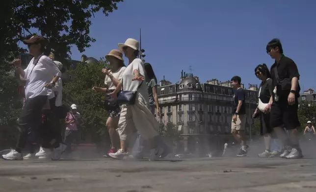 Tourists walk though fresh water vapor sprayed to the ground during a mister test, during a heat wave Monday, June 30, 2025 in Paris. (AP Photo/Christophe Ena)