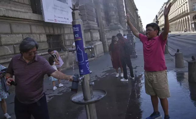 Tourists use a water fountain during a heat wave, Tuesday, July 1, 2025 in Paris. (AP Photo/Christophe Ena)