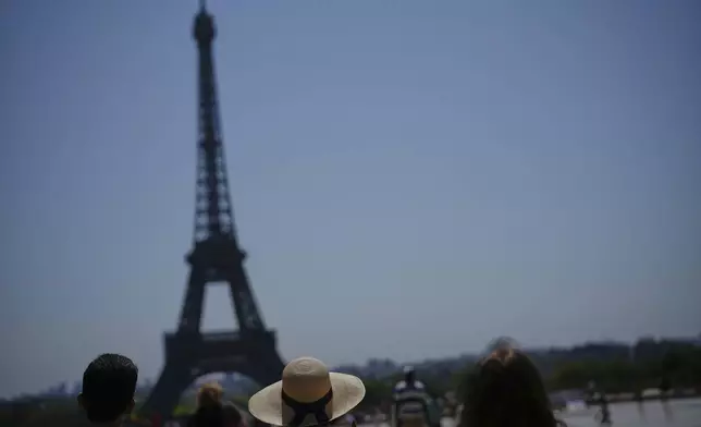 People look at the Eiffel Tower at Trocadero plaza during a heat wave in Paris, France, Wednesday, July 2, 2025. (AP Photo/Christophe Ena)
