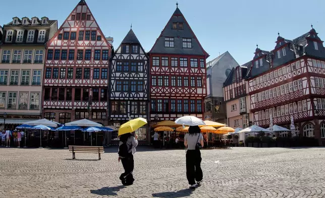 Tourist under umbrellas walk on the Roemerberg square in Frankfurt, Germany, Wednesday, July 2, 2025. (AP Photo/Michael Probst)