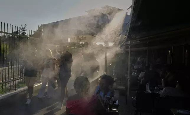 People walk past a mist machine to cool down during a hot day in the Monastiraki district of Athens, Tuesday, July 1, 2025. (AP Photo/Petros Giannakouris)