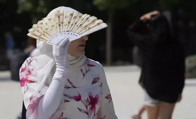 A tourist covers with a range from the hot sun in Milan, Italy, Tuesday, July 1, 2025. (AP Photo/Luca Bruno)