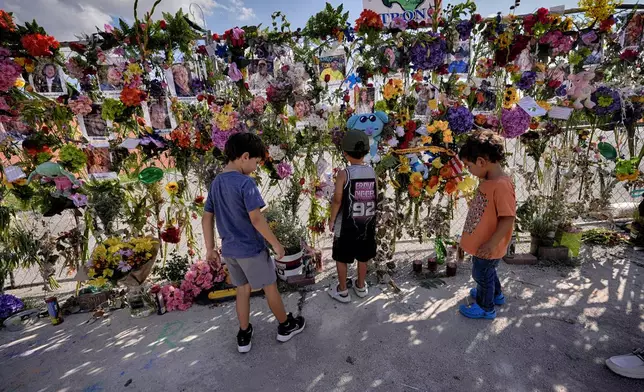 Children stand by a memorial wall of flowers and photos of flood victims prior to a vigil on Friday, July 11, 2025, in Kerrville, Texas. (AP Photo/Gerald Herbert)